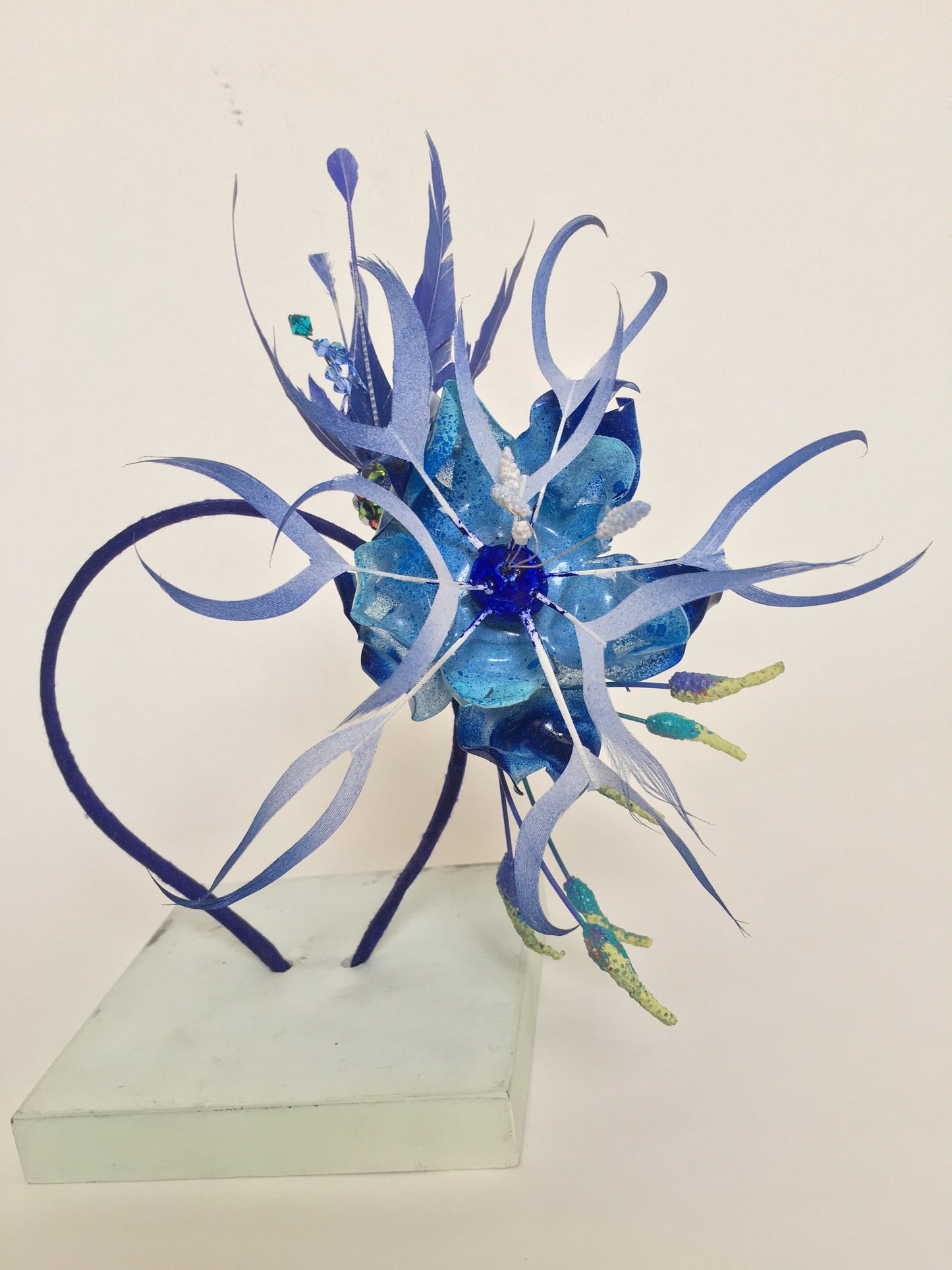 Sapphire blue feather and recycled plastic flowers on a blue silk covered band.