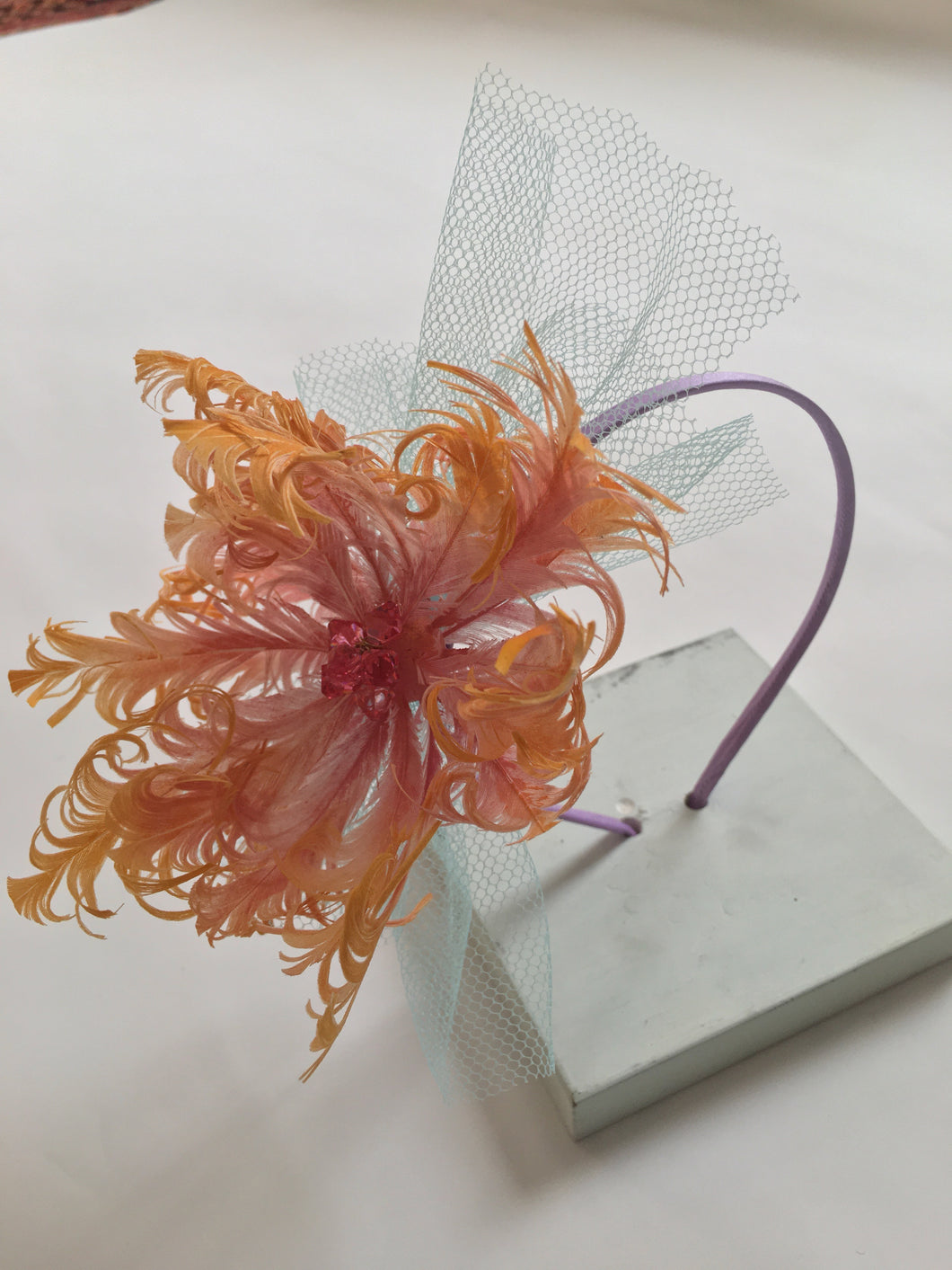 Pink and yellow feather flower with net on a lilac silk headband.